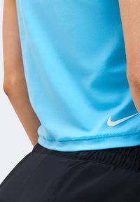 Άτομο που φοράει ανοιχτό μπλε αμάνικο μπλουζάκι Nike και μαύρα σορτς με ελαστική μέση, εμφανίζοντας το λογότυπο Nike swoosh στο επάνω μέρος του μπλουζακιού.