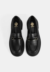 Schwarze Lederloafer mit abgerundeter Spitze, goldenen Hardware-Akzenten, gepolstertem Fußbett und stabiler Sohle; glatte Textur mit polierter Oberfläche.