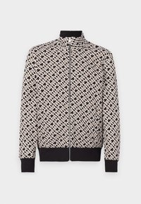 Chaqueta con cremallera de patrón geométrico en blanco y negro, con alto cuello y puños y cintura negros, exhibida sobre un fondo liso.