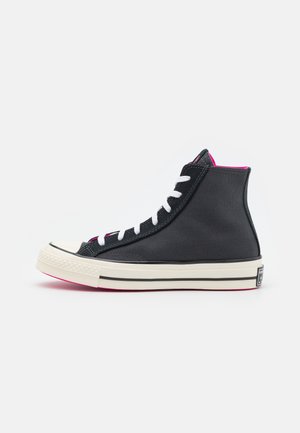 Zapatillas altas con parte superior de lona negra, cordones blancos, detalles en rosa, puntera de goma y suela blanca con rayas negras.
