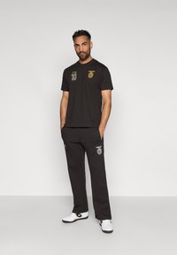 Camiseta de algodón negra con detalles dorados, que presenta un emblema de club y el número 10. Combinada con pantalones de chándal negros que muestran acentos bordados.