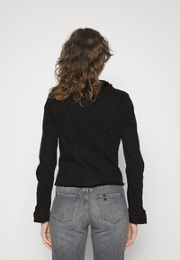 Svart denimjacka med en tight passform, fransade kanter och långa ärmar, kombinerad med urblekta grå jeans med fickor i lappar.