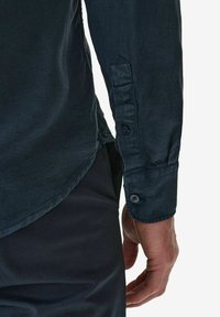 Mörkblå bomullsskjorta med spetsig krage, knappad ärm med två mörka knappar och design med rundad nederkant.