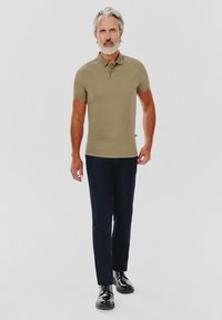 Khaki polo z kołnierzykiem, w zestawie z ciemnonawieszymi spodniami i czarnymi butami. Koszulka ma dopasowany krój i krótkie rękawy.