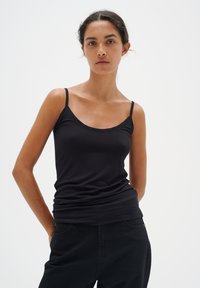 Canottiera nera con spalline sottili, scollatura a barca, design aderente e texture liscia. Abbinata a pantaloni scuri, stile minimalista.