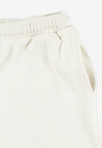 Teksturowana biała tkanina o prążkowanym wzorze, z elastycznym pasem i bocznymi kieszeniami, sugerująca wygodne ubrania do relaksu lub spodnie sportowe.