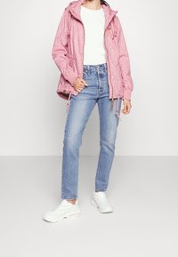 Ljusrosa jacka med blommönster, elastiska ärmslut och dragsko i midjan, tillsammans med högmidjade blå jeans och vita sneakers.