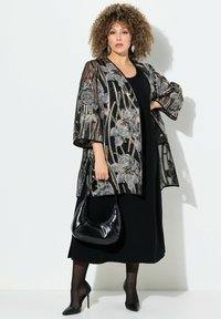 Schwarzer transparenter Kimono mit floraler Bestickung in Silber und Gold, getragen über einem schwarzen Kleid, kombiniert mit einer schwarzen Handtasche und hohen Absätzen.