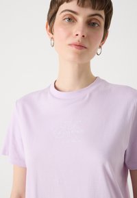 Camiseta de algodón lavanda con cuello redondo, mangas cortas y logo bordado en blanco "Calvin Klein" en el frente.