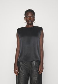 Sort satin top uden ærmer med skulderpuder, rund hals og glat tekstur, parret med sorte læderbukser. Enkel design, monokrom look.