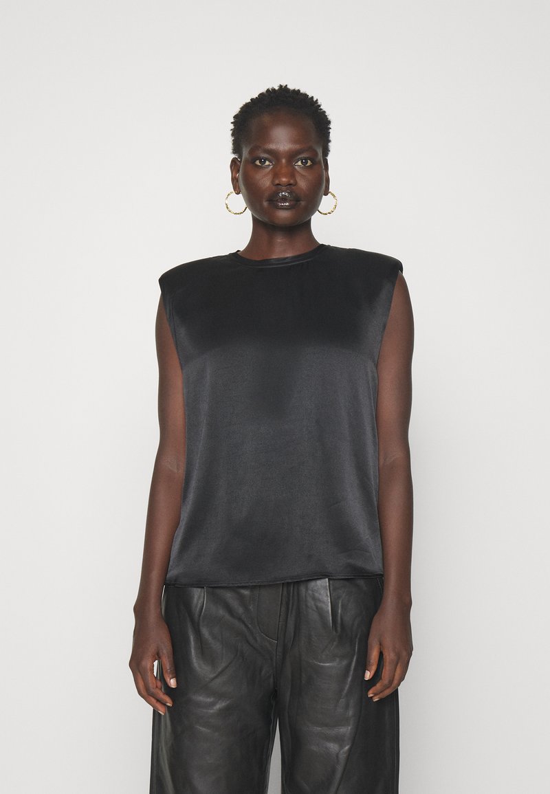 Haut sans manches en satin noir avec épaulettes, col rond et texture lisse, associé à un pantalon en cuir noir. Design simple, look monochrome.