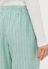 Pantaloni da pigiama a righe verde chiaro con fascia elastica in vita. Il tessuto appare morbido e leggero, con sottili righe bianche.