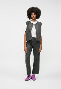 Mørk grå denimvest med trykknapper, kombinert med matchende vide bukser med subtil mønster. Modellen har på seg rosa sneakers.