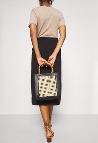 Černá kabelka čtvercového tvaru, s tkaným béžovým předním panelem a rukojetí z bambusu. Hladká textura s kontrastními vzory.