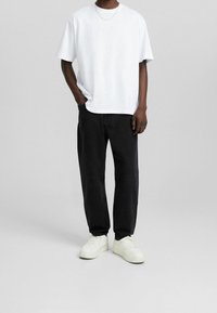 Camiseta blanca de manga corta con un corte relajado, combinada con jeans negros de corte holgado y zapatillas blancas. Diseño simple y limpio con un aspecto minimalista.