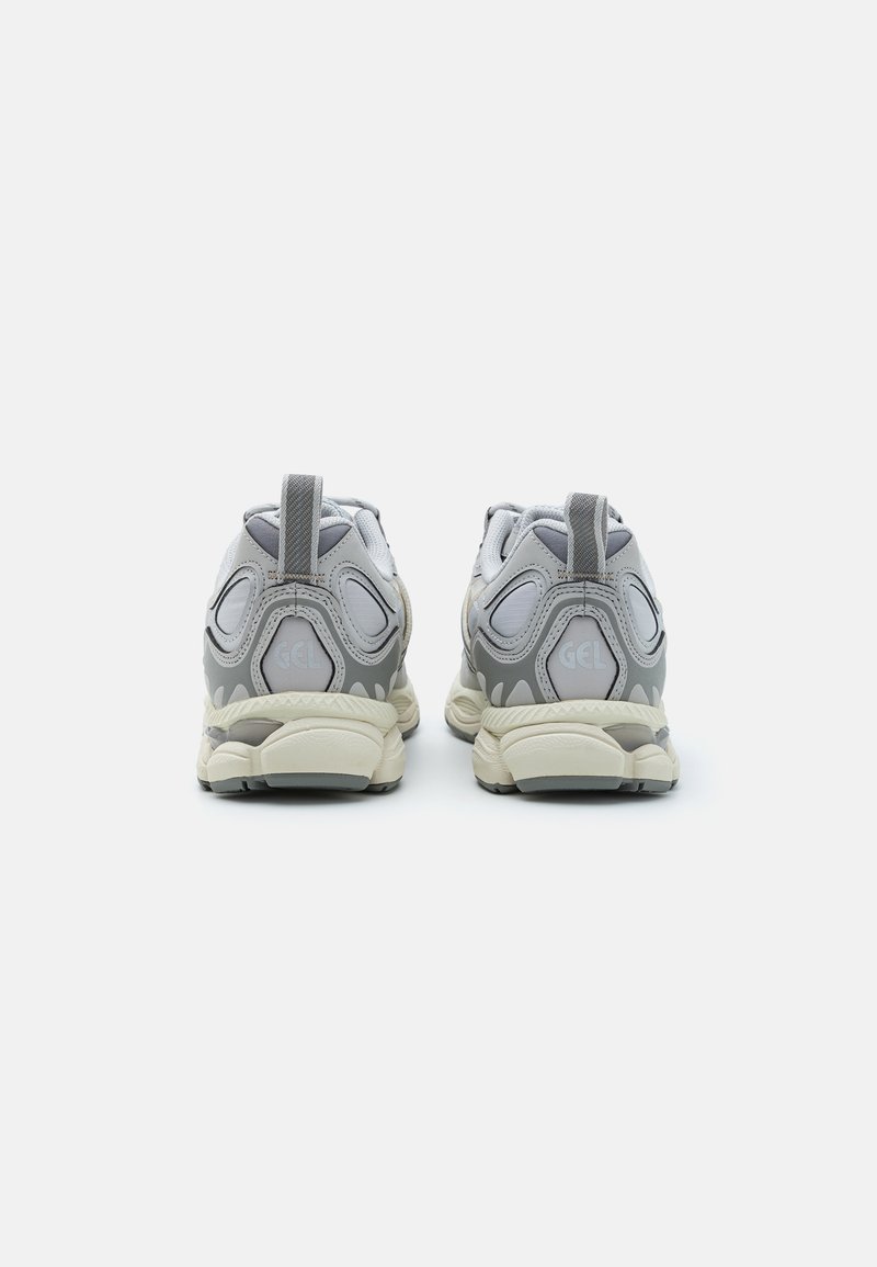 Graue und weiße Sportschuhe mit gepolsterter Sohle, Mesh- und Synthetik-Obermaterial, Zuglasche und GEL-Branding an der Ferse.