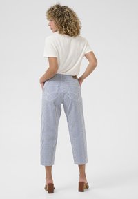 Blue and white striped trousers with a fitted waist, slight stretch, and two back pockets. Worn with a light-colored t-shirt and heels.