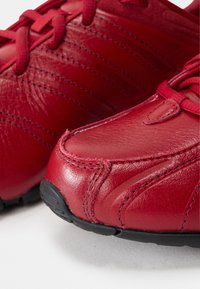 Rote Leder-Sportschuhe mit einer strukturierten Oberfläche und genähten Details, einer runden Zehenpartie und einer schwarzen Gummisohle.