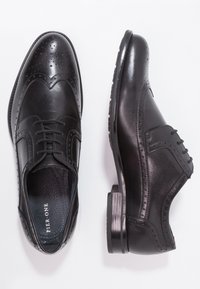 Chaussures habillées en cuir noir avec des détails brogue, une finition lisse, un design à lacets, et un talon bas avec une semelle texturée.