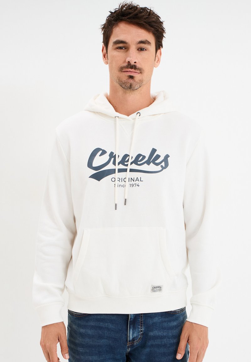 Sudadera blanca hecha de una tela suave con un bolsillo frontal, capucha ajustable con cordones y un logo en navy que dice "Creeks" en el pecho.