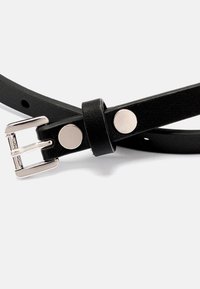 Mustakosinen vyö, jossa on hopeanvärinen metalli solki ja kaksi pyöreää metallikoristetta. Hihnassa on säädettävät reiät koon mukauttamiseen.