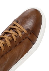 Baskets en cuir marron à la finition lisse, dotées de lacets beige, d'une semelle en caoutchouc blanc et de détails de couture minimalistes sur les côtés.