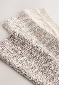 Jambières tricotées dans des tons crème et marron. Motifs texturés avec un mélange de matériaux, présentant des bords côtelés pour un ajustement amélioré.