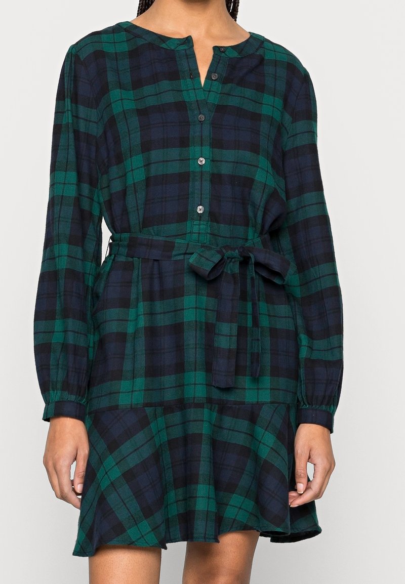 Robe à carreaux verts et bleu marine avec manches longues, boutonnée à l'avant et ceinture à la taille ; comprend une jupe évasée et un tissu texturé.