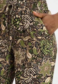Tissu noir avec un motif floral et de feuilles multicolore détaillé en vert et en beige. Présente une taille élastique avec un cordon de serrage et des poches latérales.