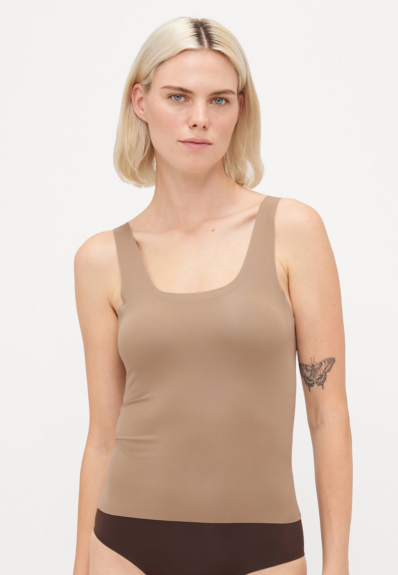Brown tank top with wide straps, made of smooth, stretchy fabric. Features a square neckline and a fitted design, paired with dark bottoms.