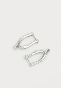 Pendientes de metal plateado con un diseño en forma de ola, que presentan curvas suaves y un borde texturizado. Primer plano del detalle del herraje visible.