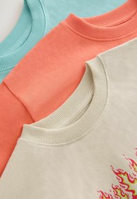 Tre sweatshirts staplade: turkos, korall och krämfärgad. Var och en med ribbad halsringning; den krämfärgade har en färgglad flamgrafik.