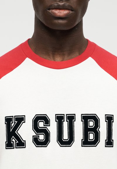 Λευκό T-shirt με κόκκινα ραγκλάν μανίκια, με μεγάλα μαύρα γράμματα "KSUBI". Κατασκευασμένο από βαμβάκι με λεία υφή και casual σχεδιασμό.