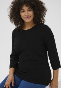 Suéter negro de punto acanalado con mangas de tres cuartos, escote redondo y corte relajado, combinado con jeans de mezclilla azul.