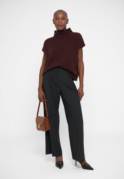 Mujer vestida con un suéter de cuello alto de manga corta color burdeos, pantalones de pierna ancha a rayas, tacones negros y sosteniendo un bolso de piel marrón.