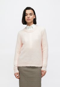 Šviesiai rožinis, minkštas megztinis su apvalia iškirpte ir ribinėmis rankogaliais, derinamas su languota suknele, pasižyminčia laisvu siluetu.