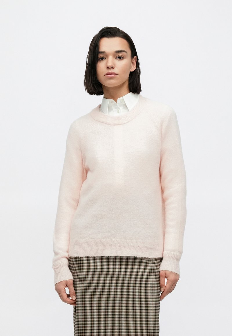 Šviesiai rožinis, minkštas megztinis su apvalia iškirpte ir ribinėmis rankogaliais, derinamas su languota suknele, pasižyminčia laisvu siluetu.