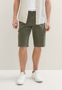 Shorts cargo de color verde oliva hechos de algodón, con múltiples bolsillos, cierre de botón y corte recto. Llevados con zapatillas blancas.