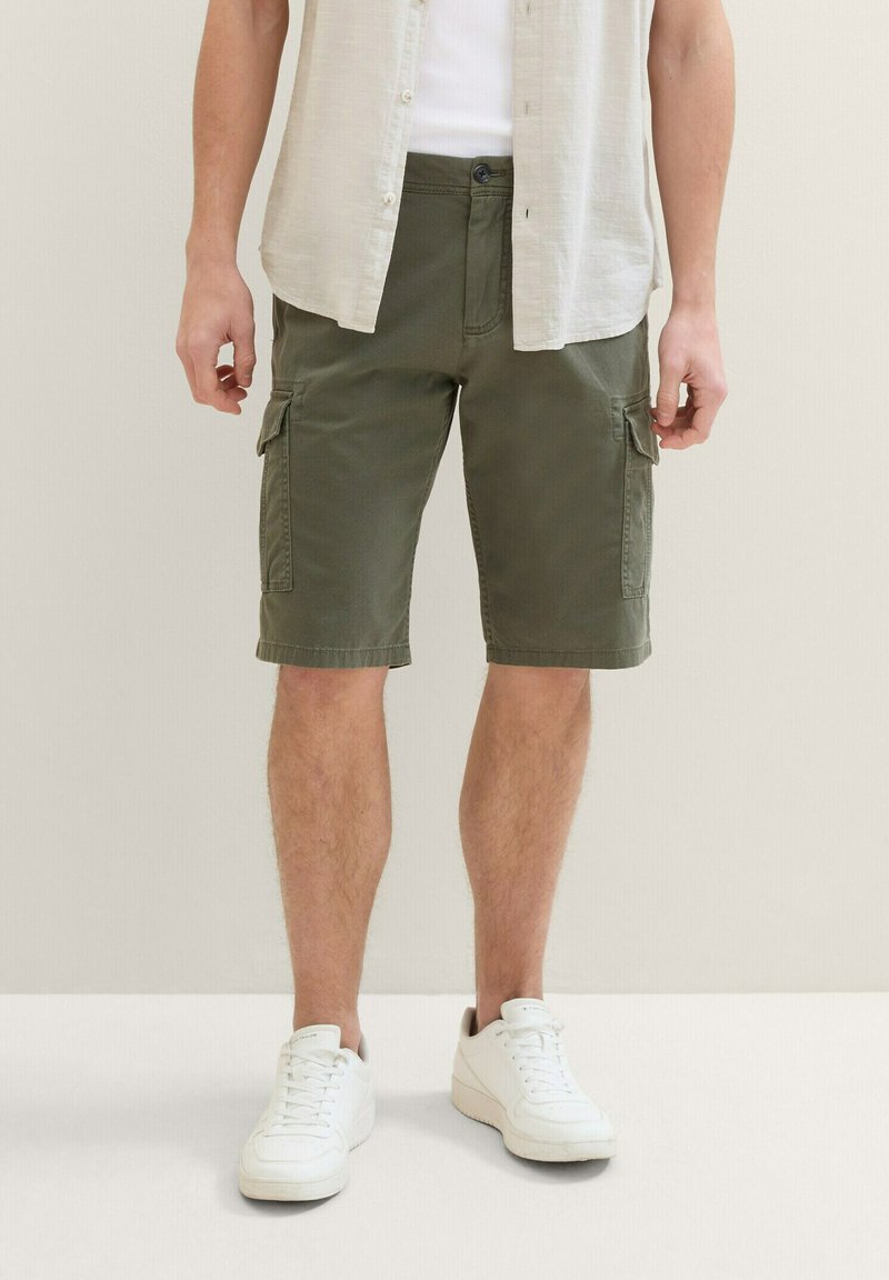 Shorts cargo de color verde oliva hechos de algodón, con múltiples bolsillos, cierre de botón y corte recto. Llevados con zapatillas blancas.