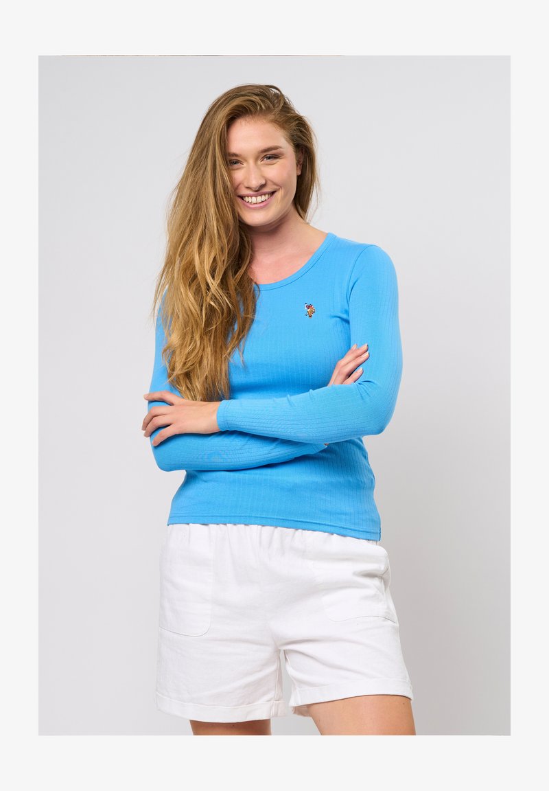 Garie ar garām piedurknēm, ribota zila blūze ar apaļu izgriezumu un nelielu izšuvumu, apvienota ar baltām šortiem ar sānu kabatām.