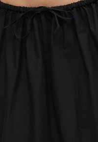 Jupe en tissu noir avec taille élastique froncée et nœud noué au centre devant.