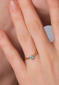 Goldring mit glattem Band und einem runden, hellblauen Edelstein, der in einer Vierkrallenfassung eingesetzt ist, der an einem Finger getragen wird.