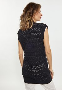 Pulover negru tricotat fără mâneci, cu modele texturate în formă de diamant, margine ondulată și o tăietură lungă care ajunge sub șolduri.