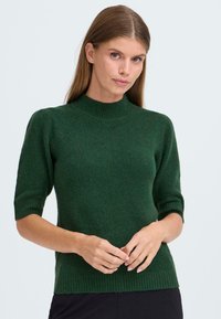 Pull tricot à manches courtes en vert foncé, avec un col montant et un ourlet côtelé. Texture douce avec une silhouette ajustée.