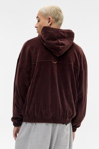 Hnědá kordová mikina s kapucí a volným střihem, ribštovou texturou a elastickým lemem. Obsahuje ventilační otvor na zádech.