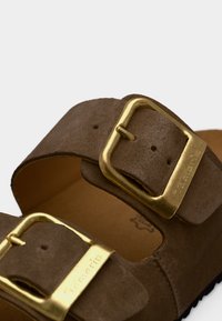 Sandale en daim marron avec deux larges brides et boucle en métal doré. Surface texturée et semelle moulée pour un confort optimal.