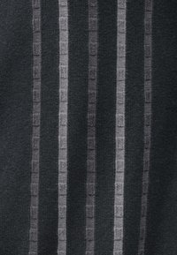 Πλεκτός ιστός με κάθετες ρίγες σε σκούρο γκρι και ανοιχτό γκρι. Το σχέδιο περιλαμβάνει μικρές τετράγωνες διακοσμήσεις κατά μήκος των ρίγων.