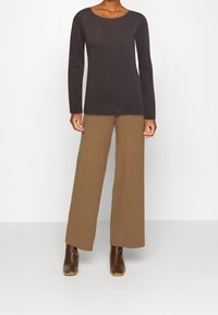 Langärmliges, dunkelgraues Oberteil mit einem runden Ausschnitt, kombiniert mit weit geschnittenen, hellbraunen Hosen und braunen Stiefeletten. Weicher Stoff, minimalistisches Design.