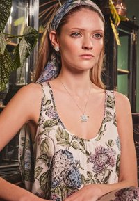 Abito senza maniche con motivo floreale in tessuto leggero, caratterizzato da fiori blu e rosa. Accompagnato da una collana con pendente a forma di fiore in argento e un foulard coordinato.