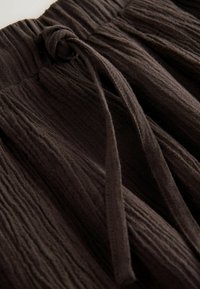 Tela arrugada de color marrón oscuro con una cintura elástica fruncida y dos lazos estrechos de tela unidos.